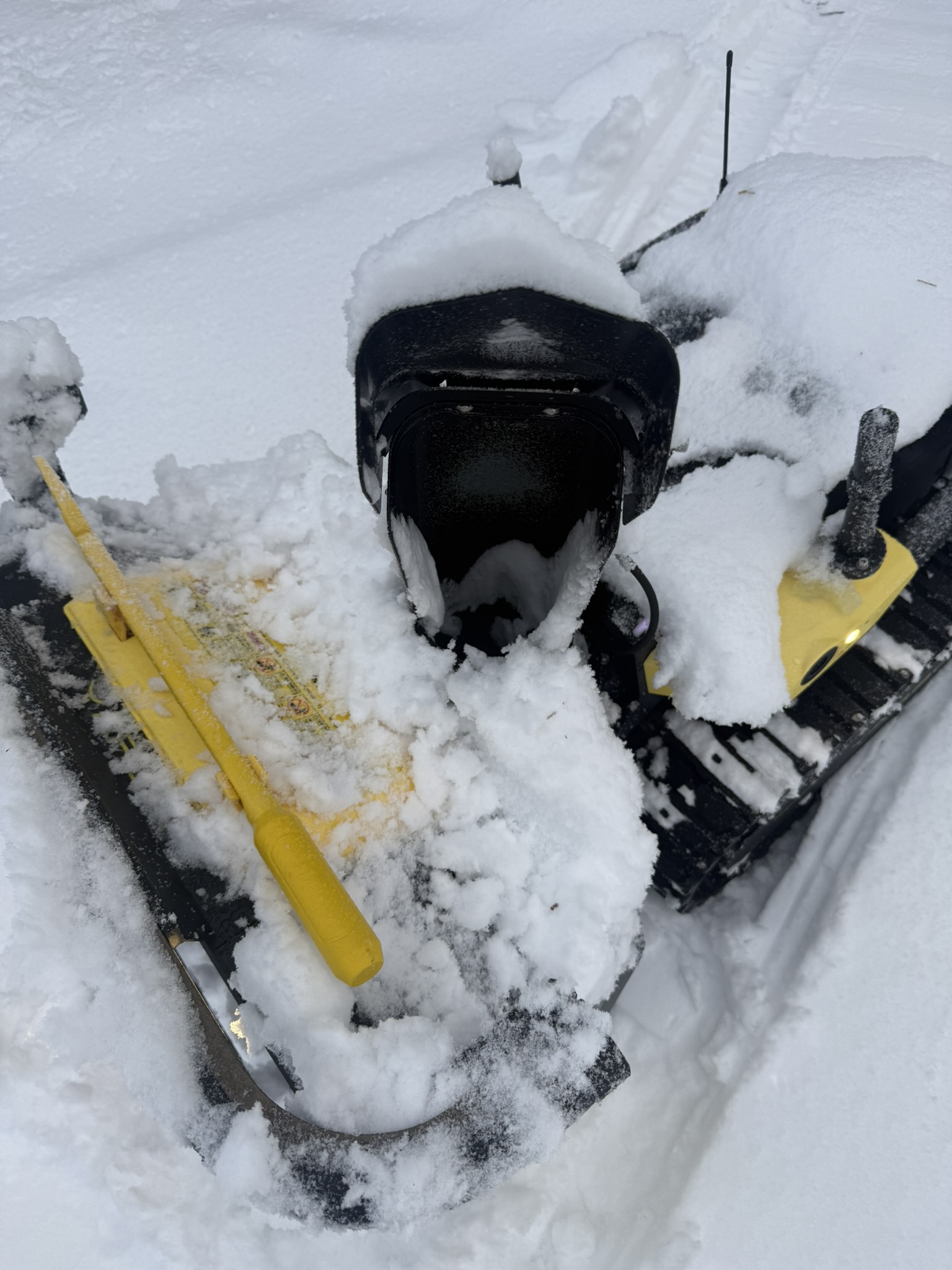 Yarbo half buried in snow next to a yellow shovel